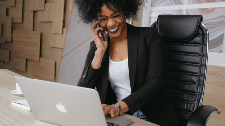 A woman sitting at a desk using her computer while chatting on the phone