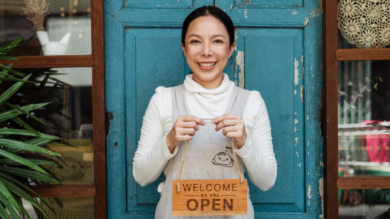 A woman who started her business standing with a welcome sign