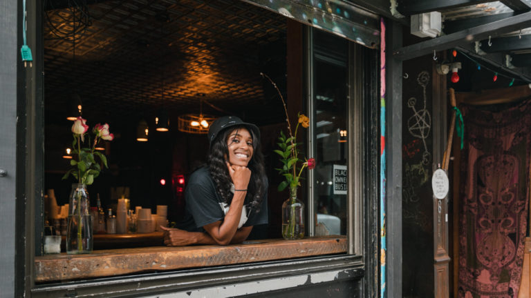 A small business owner stands leans through the open window of a business