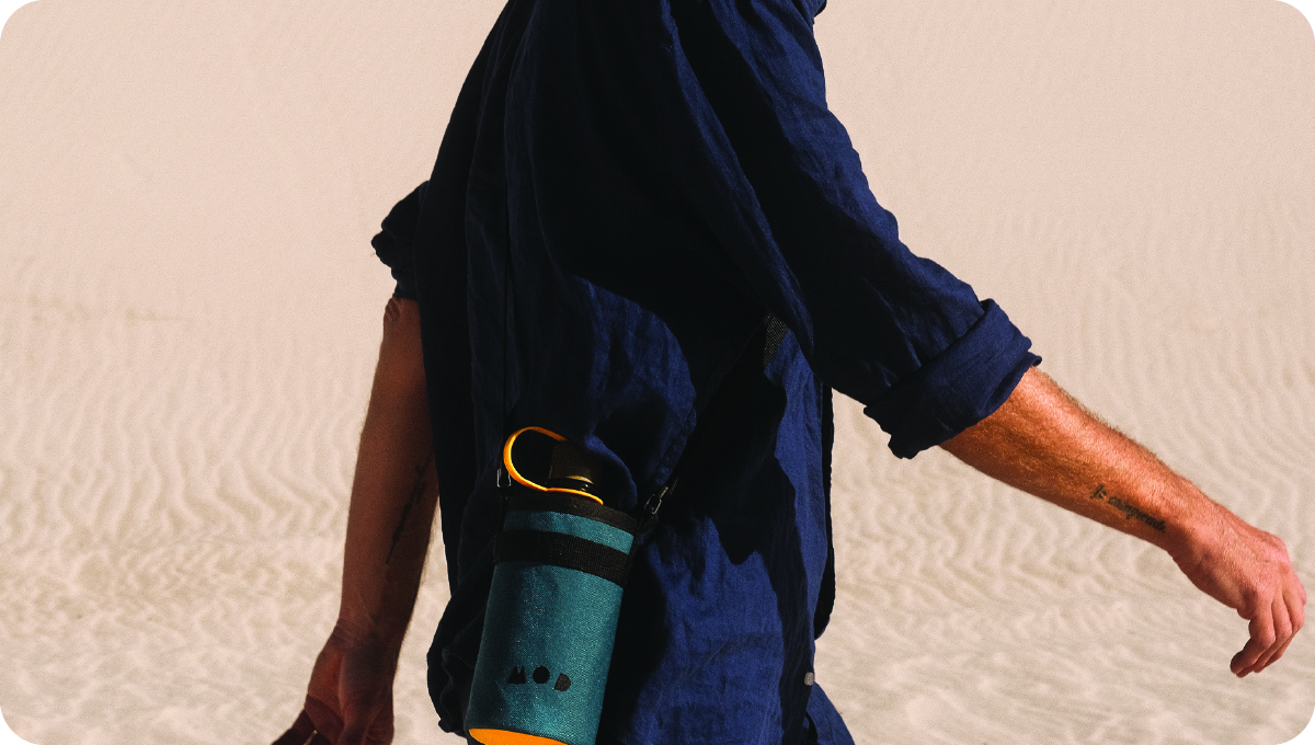 A man walking through the desert wearing a navy shirt with a MOD bottle holder slung across his shoulder.